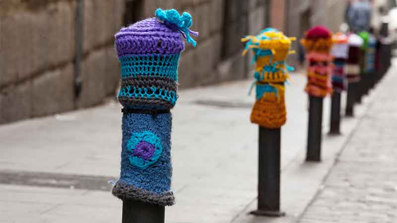 Bolardos cubiertos con tejidos de ganchillo coloridos en una calle de Madrid.